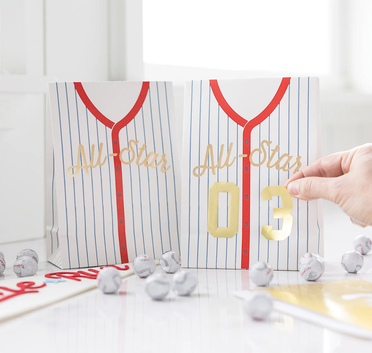 Treat bags designed like baseball jerseys, including sticker numbers for personalization at a kids' baseball party.