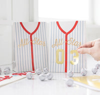 Treat bags designed like baseball jerseys, including sticker numbers for personalization at a kids' baseball party.