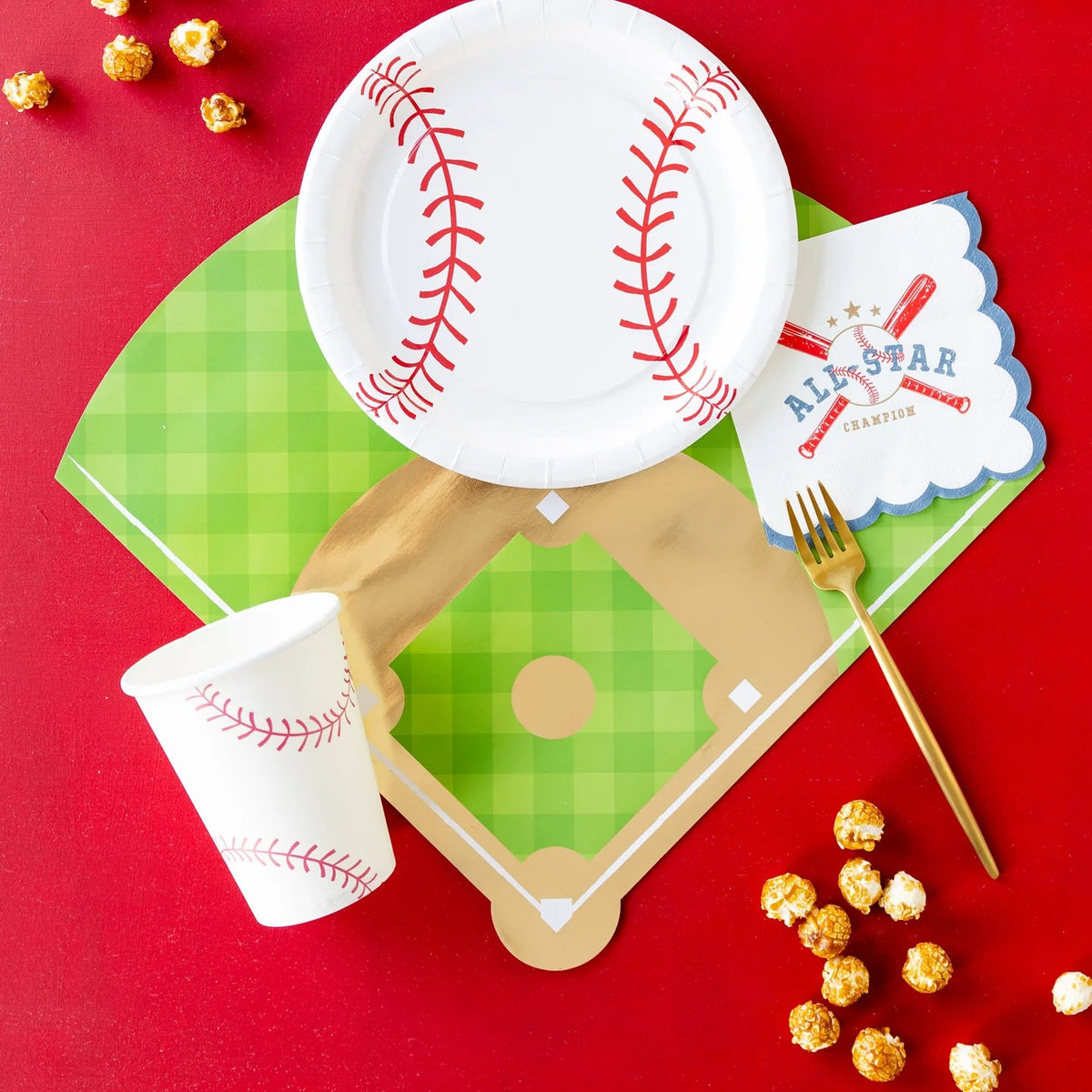 Red backdrop showing baseball diamond placemat, stitched cup, round baseball plate, caramel popcorn, and gold fork.