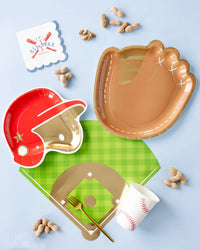 Sports‑themed tablescape on blue background featuring brown glove plate, red helmet plate, baseball cup, and peanut snacks.