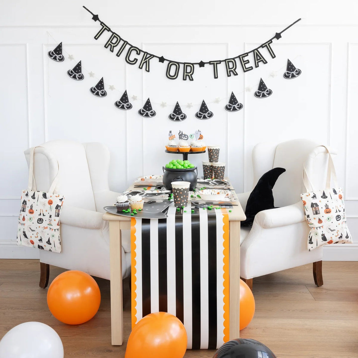 Halloween snack table with black-and-orange cups, striped runner, and Trick or Treat banner.