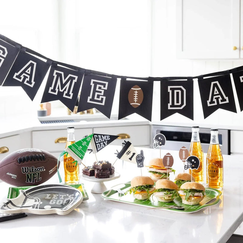 Game day football banner above mini burgers, brownies, drinks, and football party decorations