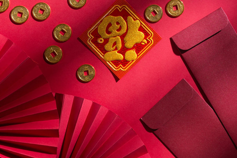 Lunar New Year decorations with red envelopes, gold coins, and paper fan on a red background