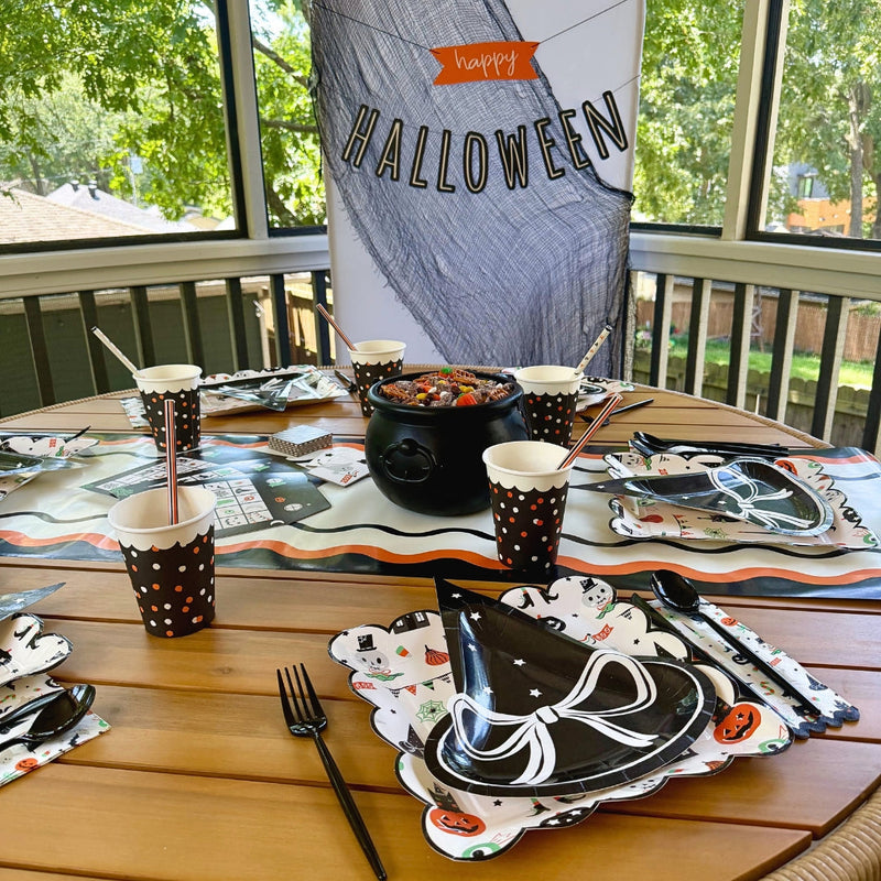 Vintage Halloween party table with black and orange tableware, Halloween plates, cups, napkins, and festive banner