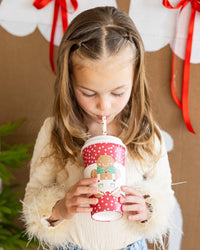 Child drinking from a red polka-dot to-go cup with a Gingerbread Straw at a Christmas party.
