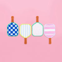 Row of four paddle‑shaped napkins on pink background: royal‑blue check, lemon‑stripe, blush gingham, and pink‑stripe designs.