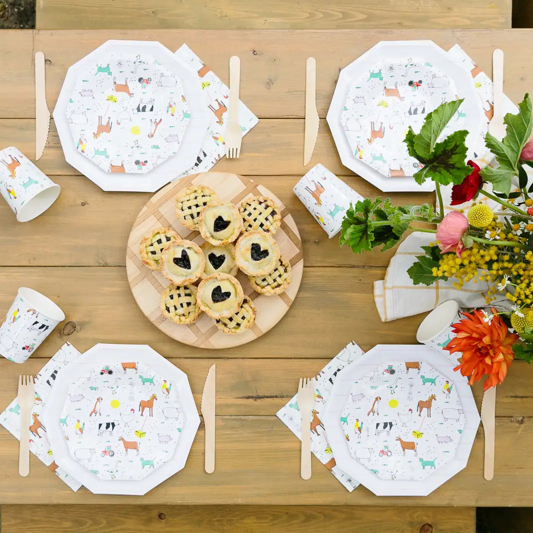 Outdoor wooden table set with farm animal plates and napkins around mini heart‑pie centerpiece.