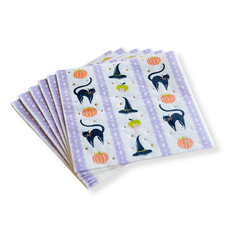 Close-up of Frills & Thrills Halloween napkins with black cat, pumpkins, and witch hat illustrations on lavender-trimmed background.