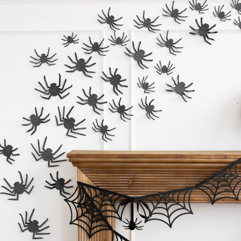 Close-up view of clustered glitter spiders crawling up a white wall above a mantel.