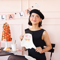 Woman in a black dress and beret holding a ghost-shaped paper plate with heart sunglasses and a beret design.