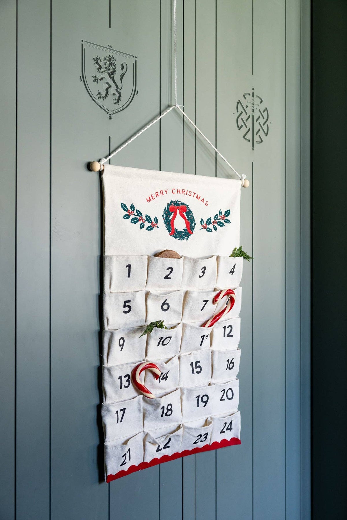 Front view of 24 pocket canvas advent calendar on green door filled with candy canes and cookies