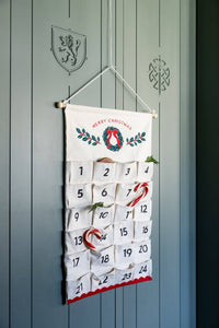Front view of 24 pocket canvas advent calendar on green door filled with candy canes and cookies