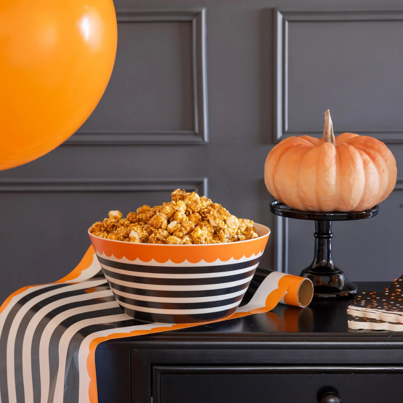 Festive black and cream striped bamboo bowl with orange scalloped edge filled with caramel popcorn, displayed on a table with Halloween décor.