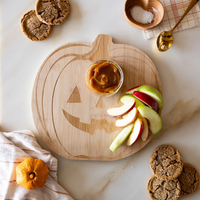 Pumpkin wood cutting board with apple slices and caramel dip for a Halloween-themed snack.