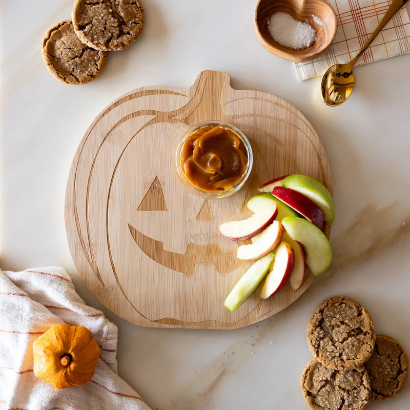 Pumpkin wood cutting board with apple slices and caramel dip for a Halloween-themed snack.