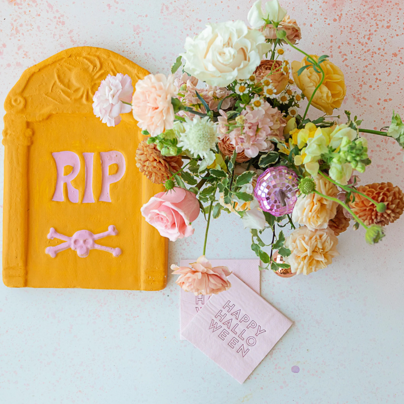 Styled Halloween scene with pastel tombstone, pink disco balls, and florals paired with Happy Halloween Pink Cocktail Napkins.