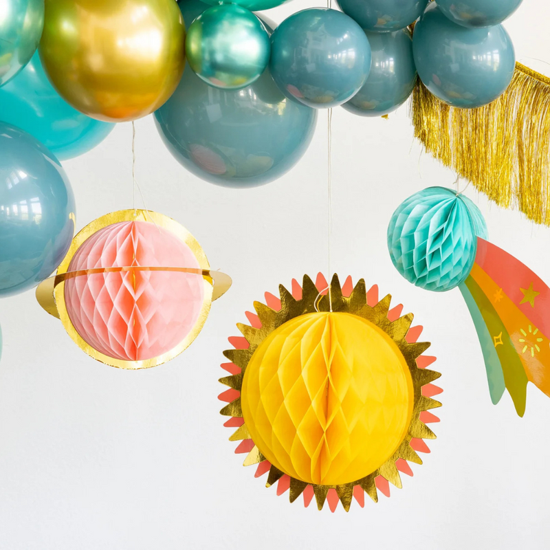Close-up of hanging decorations: pink planet, yellow sun, and teal comet