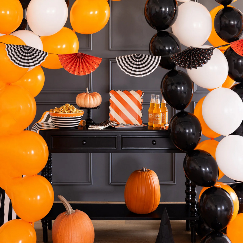 Halloween party table decorated with the Fan Bunting Banner, black table, pumpkins, balloons, and treats.