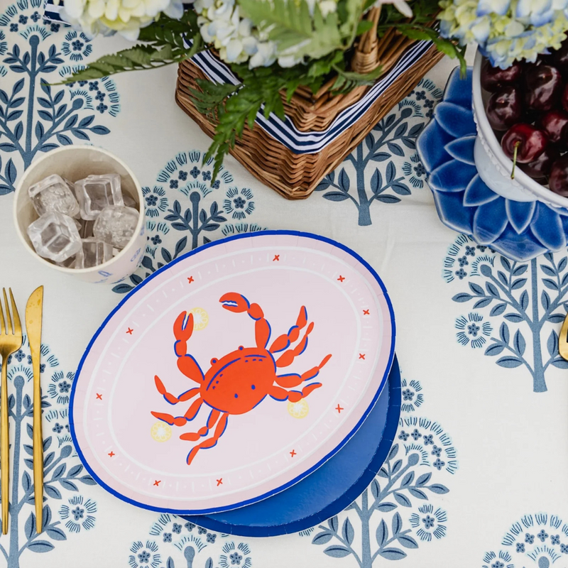 Crab-themed oval charger plate styled on a blue-and-white table setting with gold cutlery.