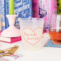 A stylish "book lover" flex cup filled with a beverage, placed on a vibrant book club table setting featuring colorful books and decorative items in the background.