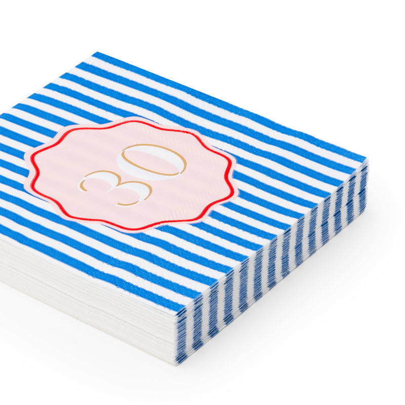 Angled stack of blue and white striped 30th birthday cocktail napkins with pink gold foil number 30 scalloped medallion on white background