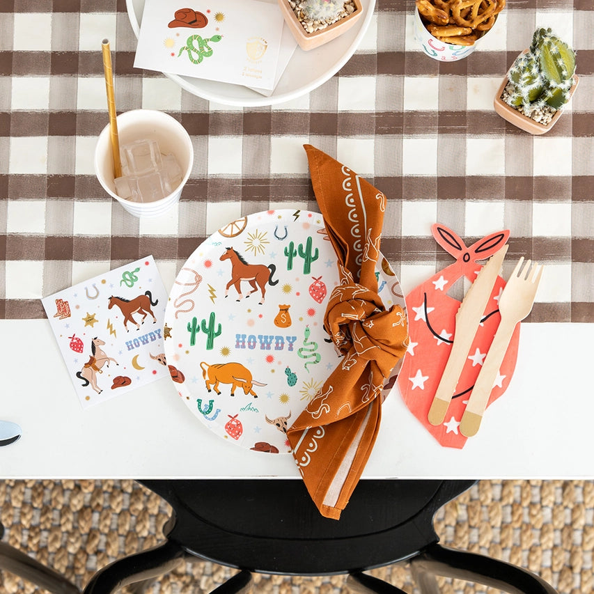 Orange cowboy‑hat plate layered on striped plate with red bandana utensil holder and disco‑ball centerpiece.