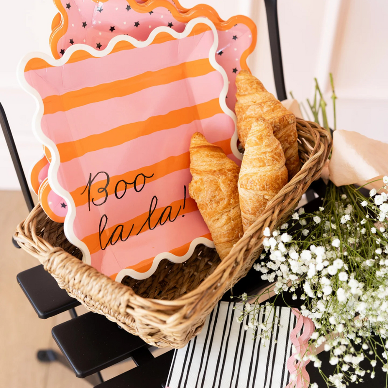 Close-up of a basket display featuring Boo La La pink striped dinner plates and striped napkins tucked beside croissants.