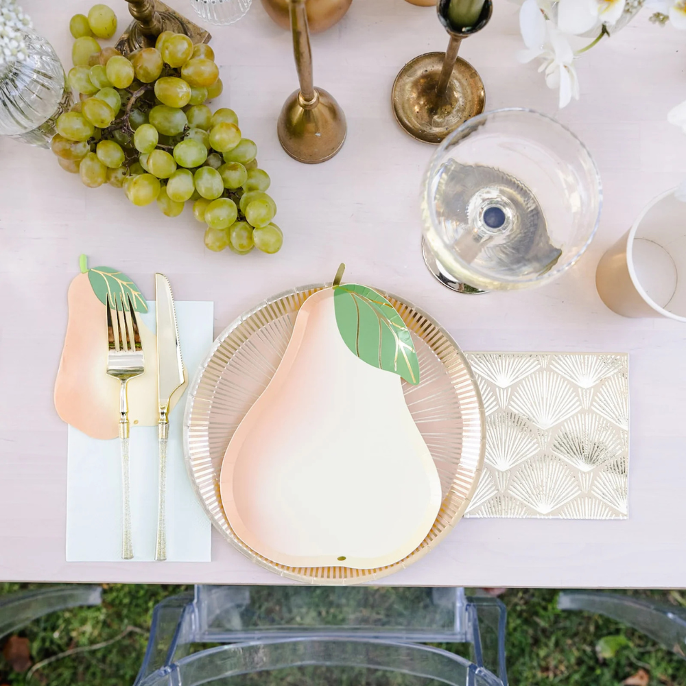 Le Dinner Pear Large Napkins styled on a table with coordinating pear-shaped plates and gold cutlery