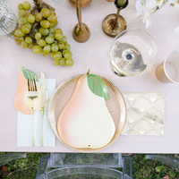 Le Dinner Pear Large Napkins styled on a table with coordinating pear-shaped plates and gold cutlery