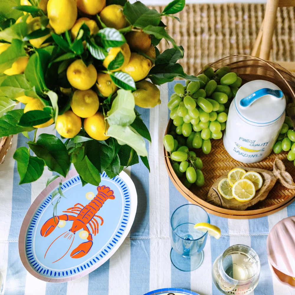 Coastal-themed table with Le Dinner Lobster Platter Charger Plate surrounded by lemons and grapes.
