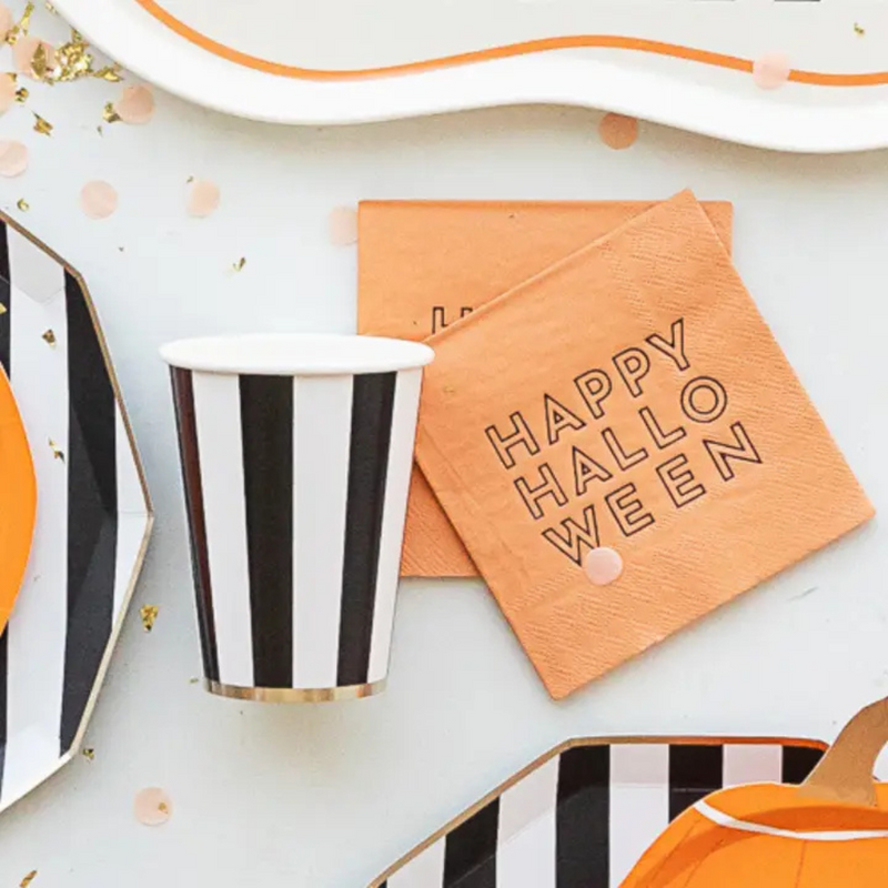 Close-up of a striped party cup beside orange cocktail napkins with “Happy Halloween” text.