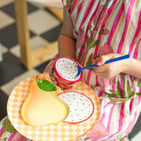 Child holding a fresh dragon fruit over a plate set with Le Dinner Dragon Fruit Cocktail Napkins
