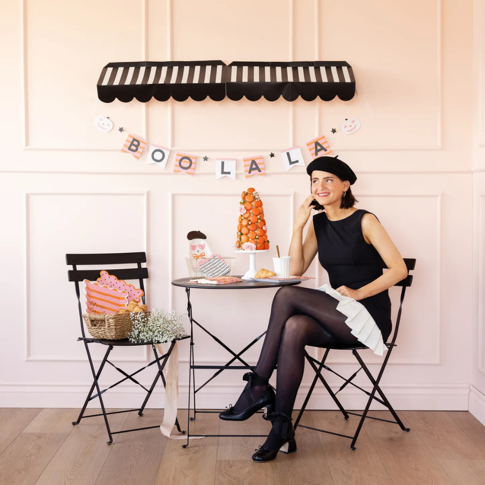 Woman in chic black dress sitting under the Boo La La Banner displayed on a pink wall