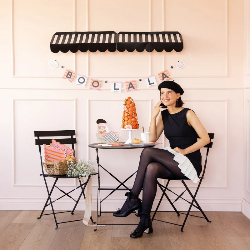 Woman in chic black dress sitting under the Boo La La Banner displayed on a pink wall