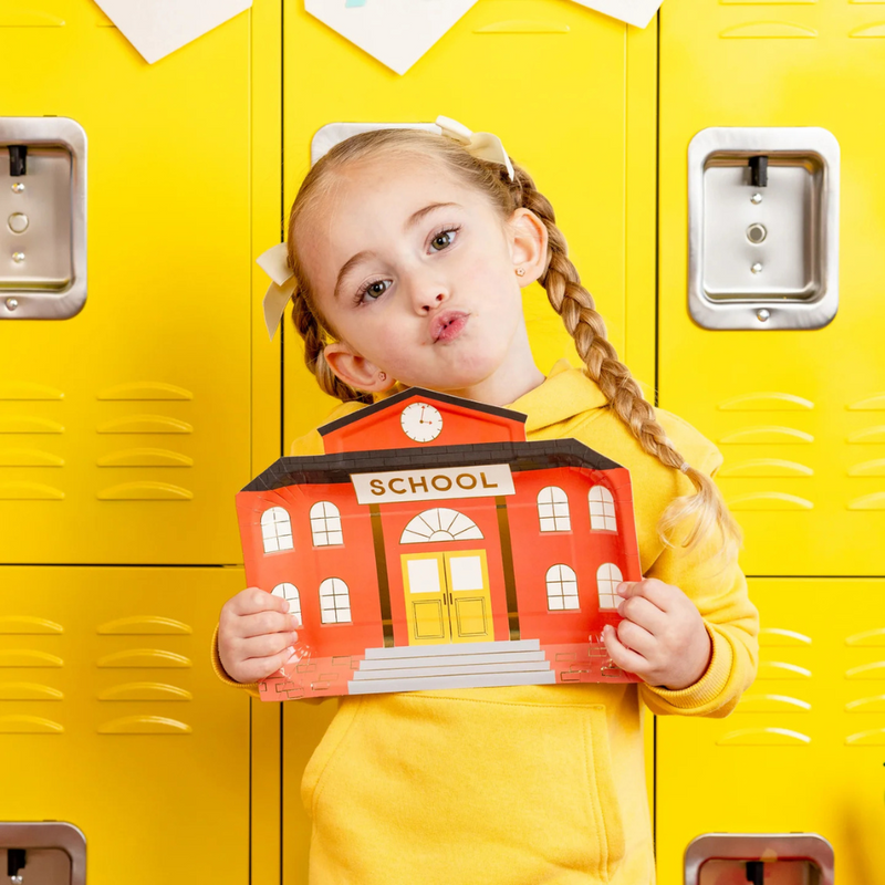 Young girl holding the school house plate in front of bright yellow lockers