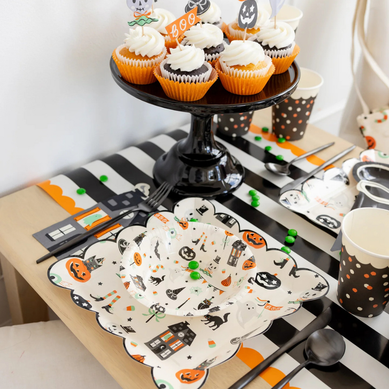 Close-up of cupcakes and Halloween tableware on black and white striped paper table runner with orange scalloped edges.