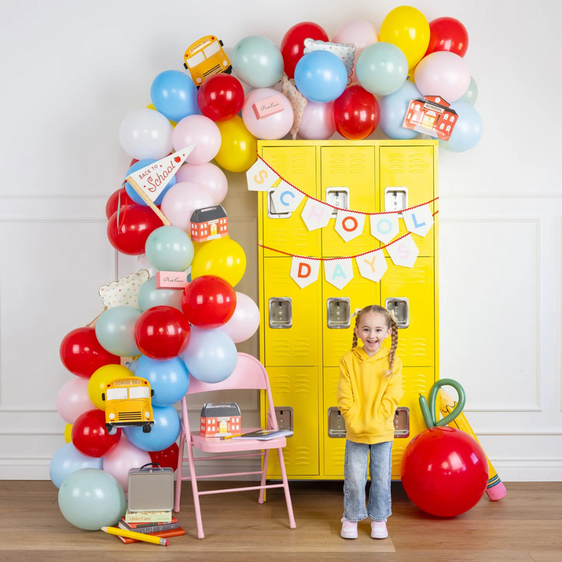 Girl standing in front of yellow lockers with back-to-school decor, Scattered Alphabet plate visible in balloon arch