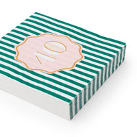Angled stack of hunter green and white striped 40th birthday cocktail napkins with pink gold foil number 40 scalloped medallion on white background