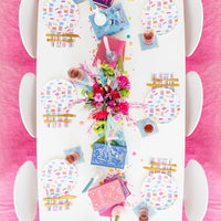 Overhead view of bright pink-accent book club table with book-pattern dinner plates, novels, floral centerpiece, and pink drink cups