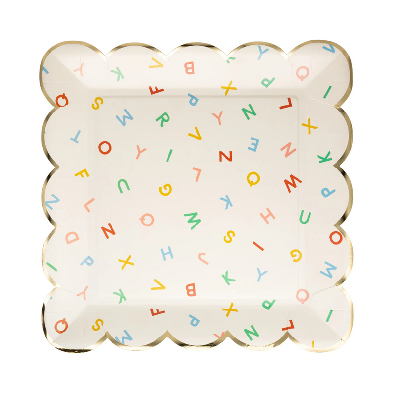 Flat lay of square paper plate with scattered colorful letters and scalloped gold foil edges