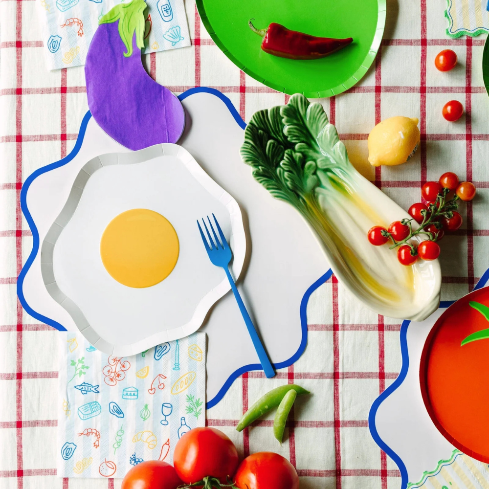 Le Dinner table setting with napkins, plates, and fresh produce decor.