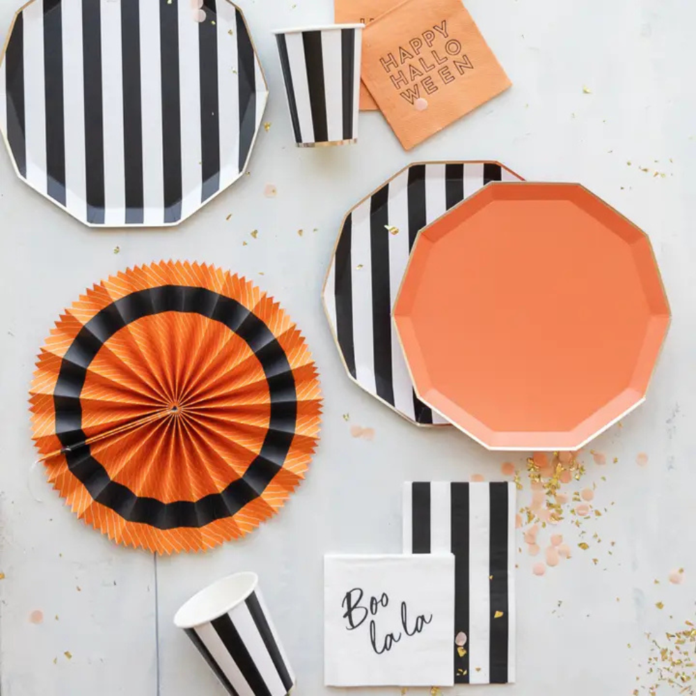 Overhead flat lay of a Halloween party setup featuring striped tableware, orange napkins reading “Happy Halloween,” and festive decorations.
