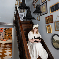 A girl in a white dress sitting on stairs decorated with three light-up witch hats floating above.