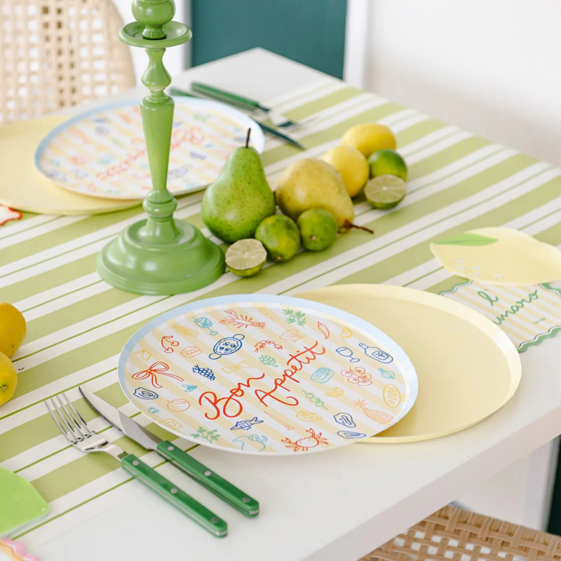Table set with Le Dinner Bon Appetit Dinner Plates alongside green candlesticks, pears, limes, and lemons.