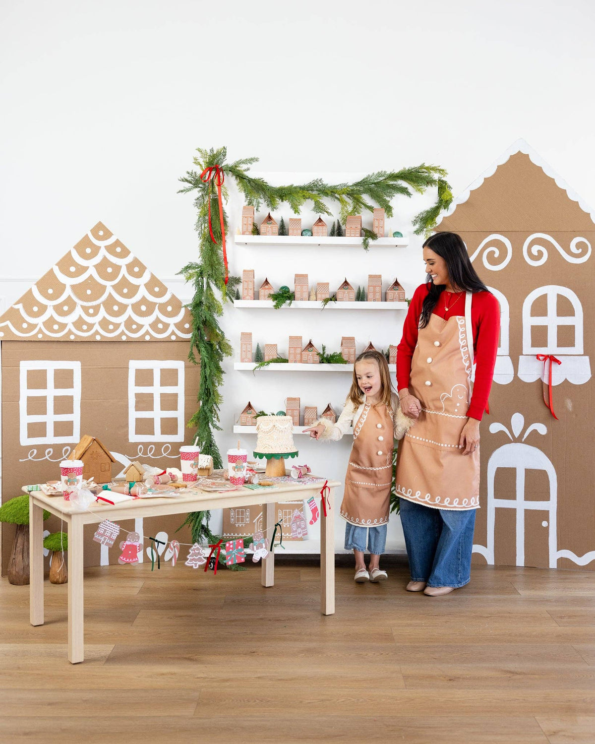 Adult and child wearing matching gingerbread aprons while baking at a festive Christmas setup with cookies and holiday décor.
