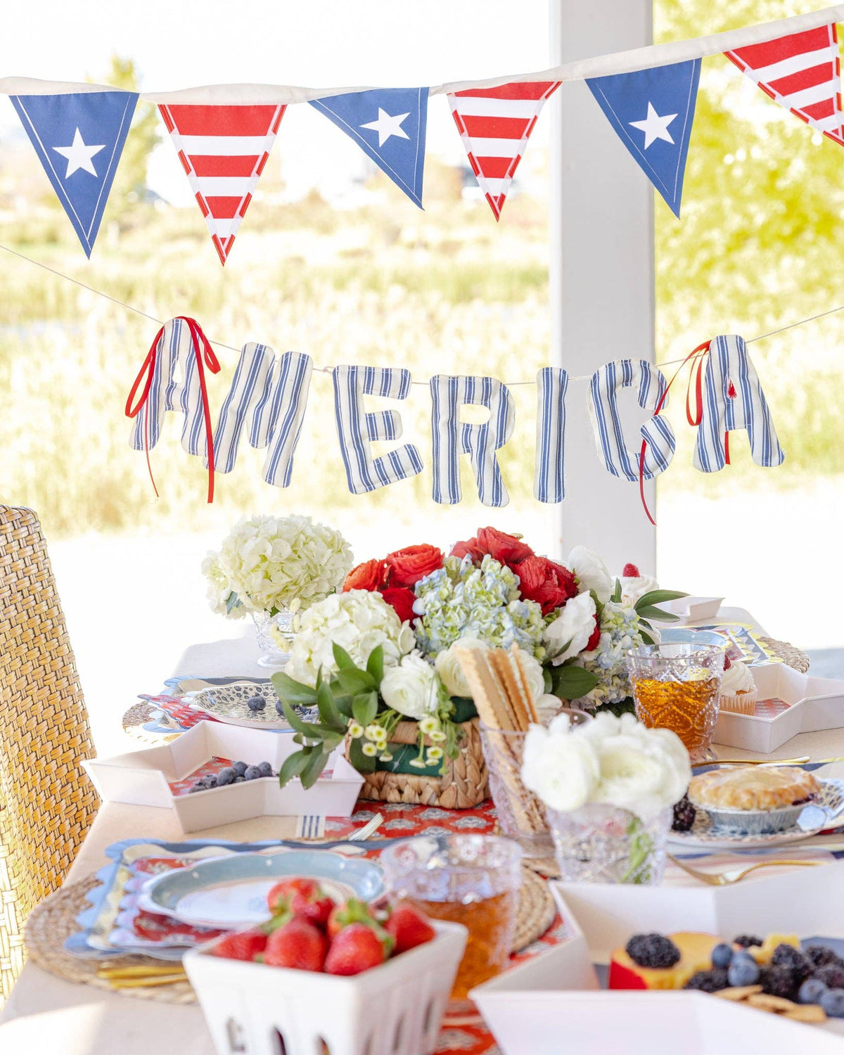 America fabric letter banner styled above 4th of July dessert table with hydrangeas and star trays