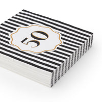 Angled stack of black and white striped 50th birthday cocktail napkins with white gold foil number 50 scalloped medallion on white background