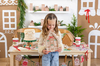 Child looking down and smiling while holding a Ginger House Plate in front of a decorated table.