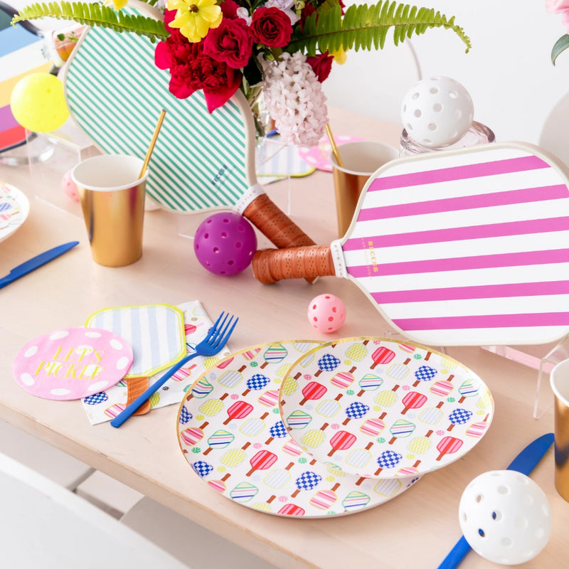 Table set with multicolor paddle dinner plates, gold cups, striped paddles as décor, and scattered pickleballs.