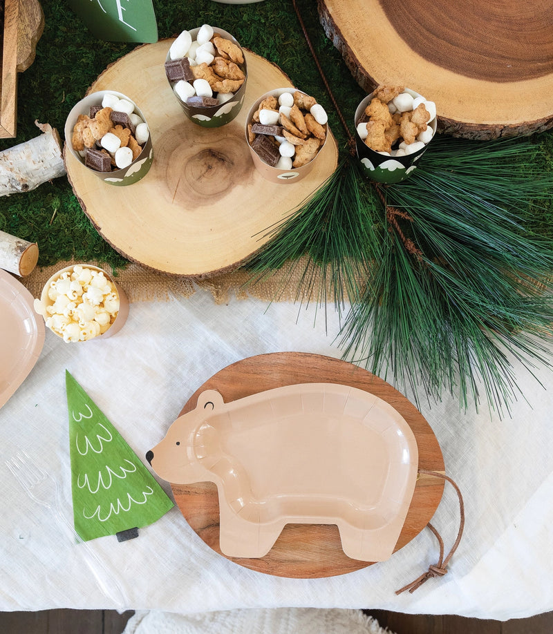 Bear plate placed on a wood slice charger with green pine tree napkin and party snacks surrounding it